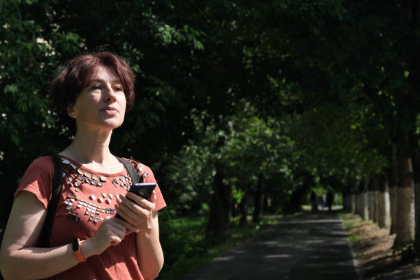 istock Mature woman is using smart phone while standing on city street 1330353612