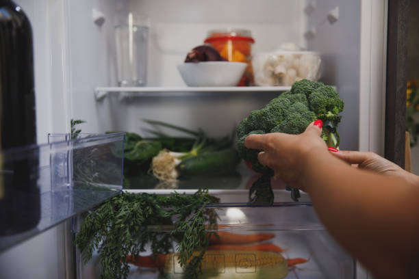 istock Female hands putting a head of broccoli in the fridge 1330360077