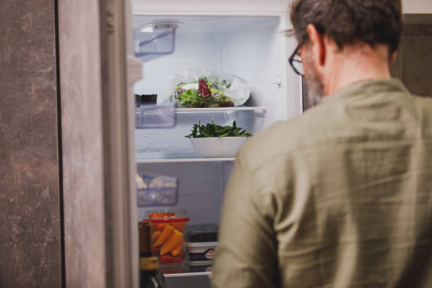 istock Rear view of man standing in front of an open fridge 1330360081