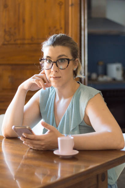 istock Young woman with glasses drinking coffee and using cell phone. Looking at the camera 1330362271