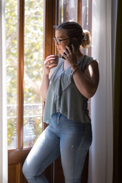 istock Young woman talking on smartphone near window 1330362418