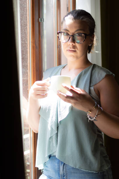 istock Beautiful young woman drinking coffee and looking through a window. 1330362423