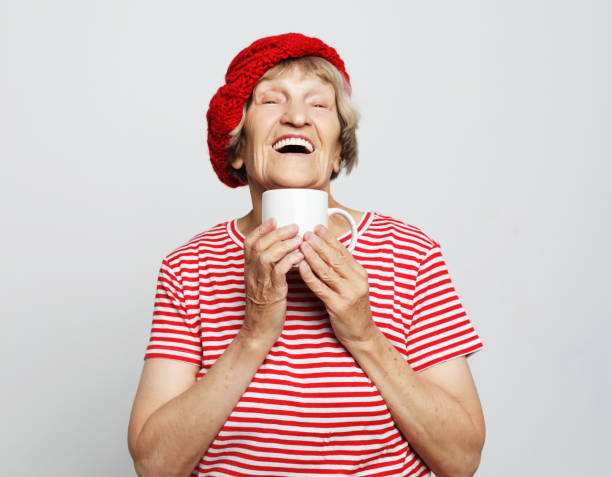 istock old excited lady smiling laughing, holding cup drinking coffee 1330367161