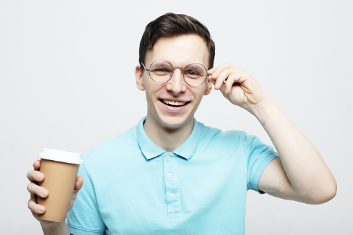 Hipster man standing with takeaway coffee, happy carefree handsome guy in eyewear isolated over white background