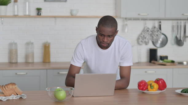 istock Attractive African Man Working on Laptop in Kitchen 1330373923