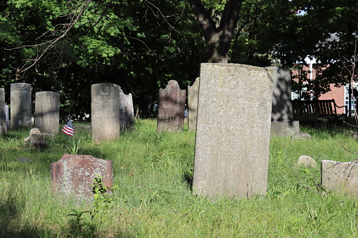 Worn and weathered tombstones in a tree-shaded revolutionary war era cemetery