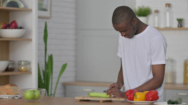 istock Healthy African Man Cutting Cucumber in Kitchen 1330374106
