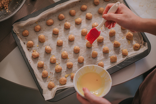 directly above top angle asian chinese mid adult woman hands brushing egg yolks on peanut biscuit on baking tray at home in the kitchen