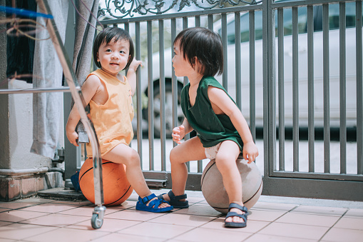 asian chinese twin baby boy sitting on basket balls in front of house during summer weekend