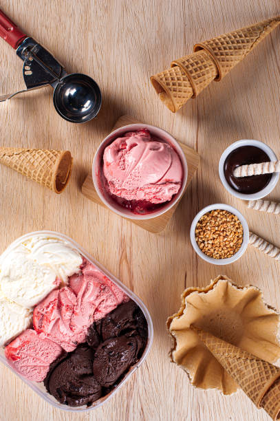 istock Three flavors of ice cream in a delivery container, making a composition with a strawberry ice cream container and several cones. Top view 1330390191