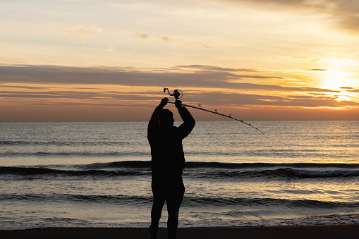 man fishing on the beach from the sand at sunrise