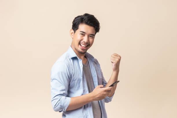 Portrait young Asian man handsome smile using smartphone in studio. Portrait young Asian man handsome happy smile in formal shirt using smartphone trading or chatting on brown isolated studio background. male chinese student stock pictures, royalty-free photos & images