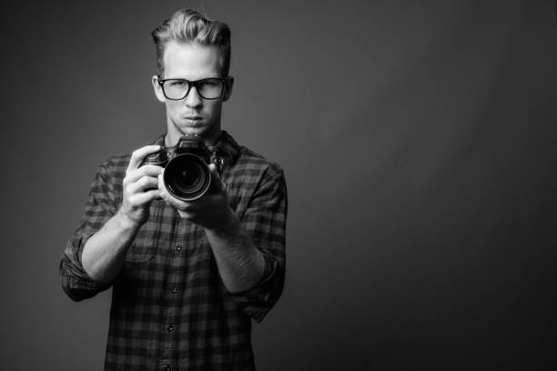 Studio shot of young handsome hipster man against gray background in black and white