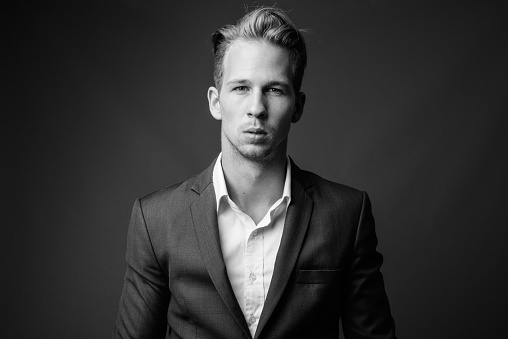 Studio shot of young handsome businessman in suit against gray background in black and white