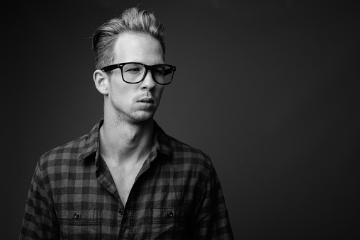 Studio shot of young handsome hipster man against gray background in black and white