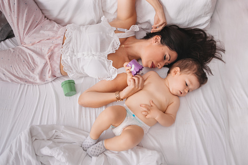 A young mother sleeping next to her baby boy in a diaper while cuddling him