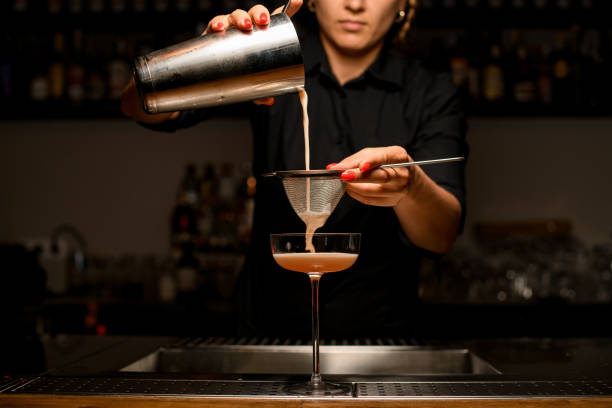 istock Woman bartender pours drink into glass by filtering it through sieve. 1330413891