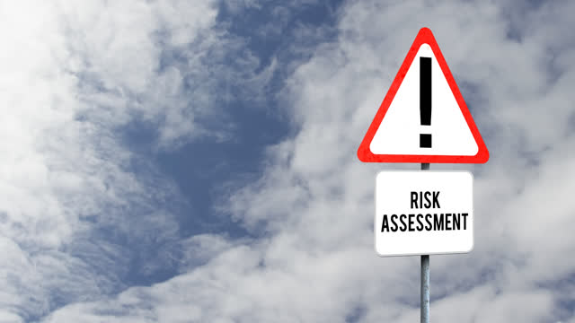 Attention signboard post with risk assessment text against clouds in the blue sky