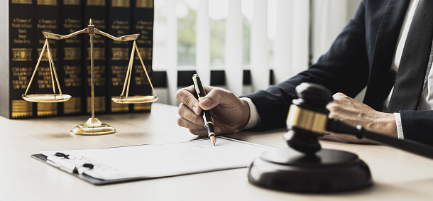 A male lawyer is signing a plea agreement with a client in a fraud case, in which the client has filed a lawsuit against an employee at a company that commits the fraud. Fraud litigation concept.