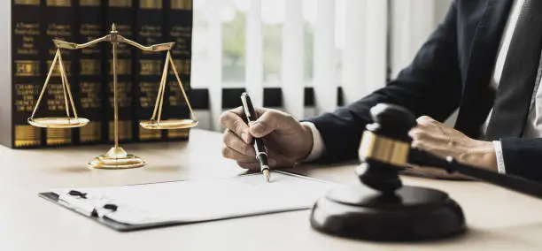 Photo of A male lawyer is signing a plea agreement with a client in a fraud case, in which the client has filed a lawsuit against an employee at a company that commits the fraud. Fraud litigation concept.