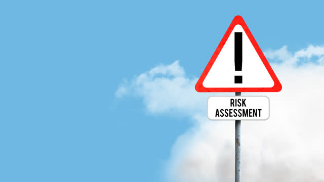 Attention signboard post with risk assessment text against clouds in the blue sky