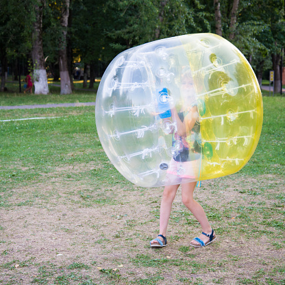 A child in a bumperball. Legs in shorts are visible from an inflatable ball. Fun on the summer lawn.