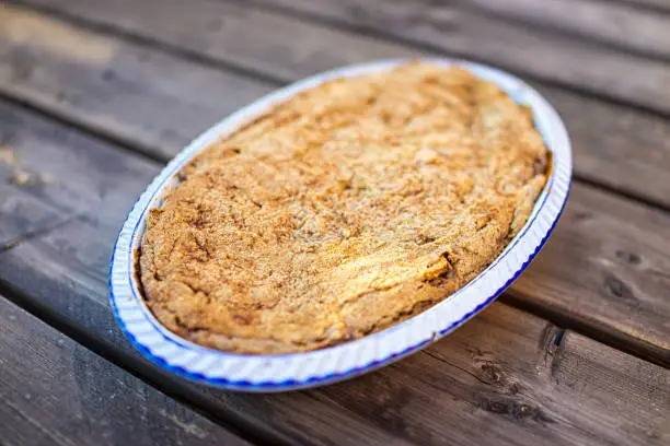 Outside wooden table and closeup of whole apple fruit pie baked dessert in blue ceramic baking dish with fruit filling and golden crust