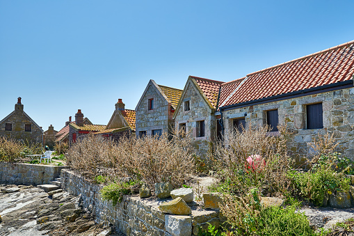 Image of the huts at Les Minquiers, Ile Maitre Island with a clear blue sky and calm sea. Jersey CI