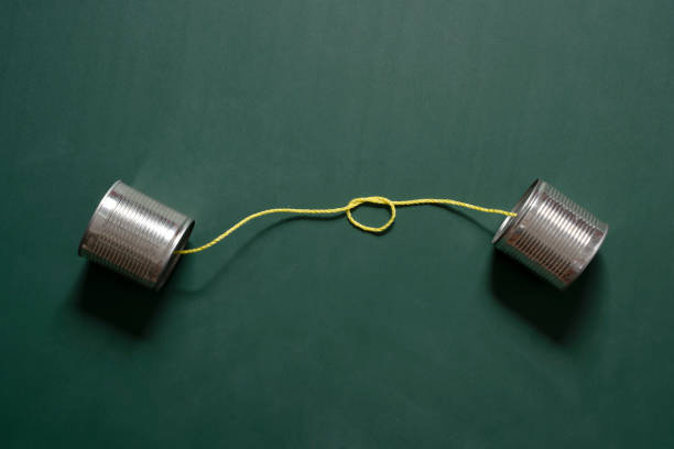 жестяные банки, ограниченные веревкой на фоне зеленого дерева - telephone can communication tin can phone стоковые фото и изображения