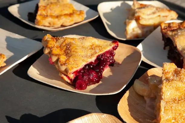 yummy slices of fruit pies (apple, berry, and cherry) sitting on a table. Red berries spilling out of center piece