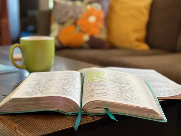 Bible Study time with bible open on table, lime-green coffee cup and pillows on the couch in the soft focus background