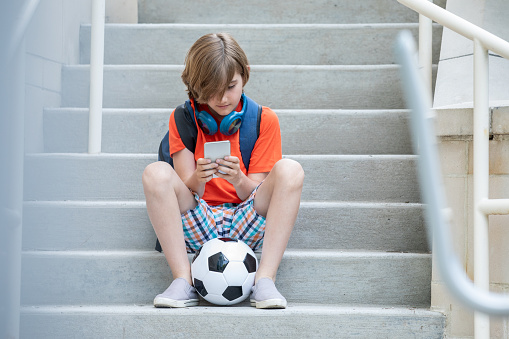 Portrait of middle aged boy sitting on the stairs texting on his phone