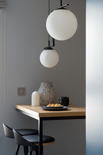 Stylish decorations on wooden table with two black chairs under modern pendant lamps