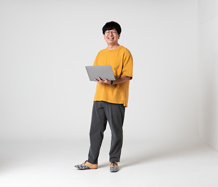 Japanese man in yellow holding a laptop in front of a white background. Taken at a photography studio in Tokyo, Japan.