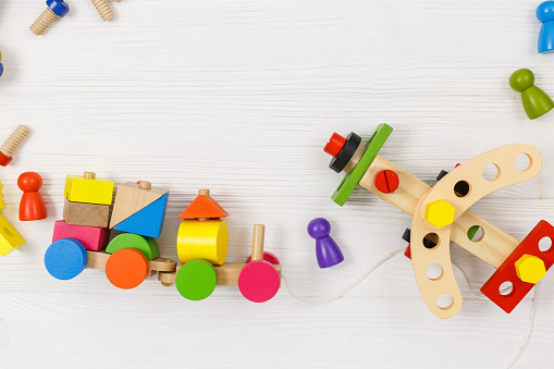 A colorful wooden building kit, train, plane for children on wood. Set of tools on white wooden table. Games and tools for kids in kindergarten, preschool or daycare. Natural, eco-friendly toys.