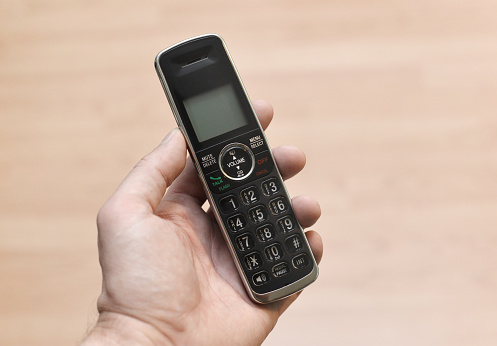 Closeup of a mass produced cordless telephone in a man's hand.