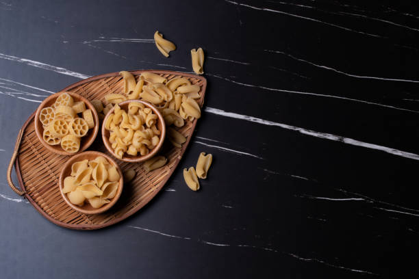 istock Raw pasta in a wooden cup on black marble background.Copy space 1330472230