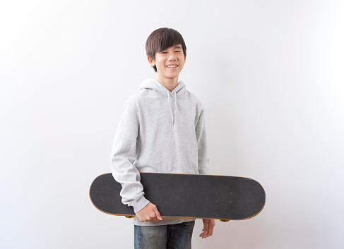 Asian teen boy holding skateboarding standing isolated on white background.