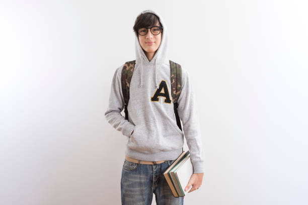 istock Handsome teen boy students carrying a backpack and books standing on white background. 1330482812