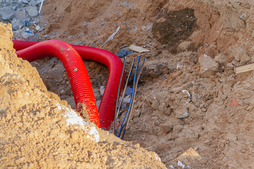 Laying an insulating plastic pipe with an electric cable underground during the construction of a house.