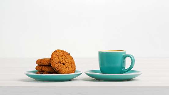 Oatmeal cookies with chocolate crumb and cup of coffee espresso on white wooden table. Front view. Copyspace.