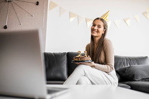 Beautiful woman celebrating her 21's birthday with friends on video call at home