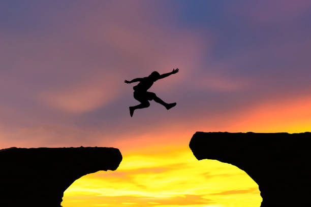 istock Men jump cliff sun light over silhouette concept 1330491269