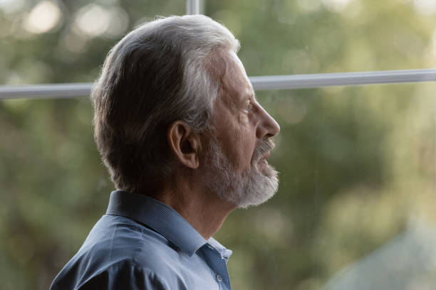 istock Sad senior 70s man lost in thoughts looking out window 1330499335