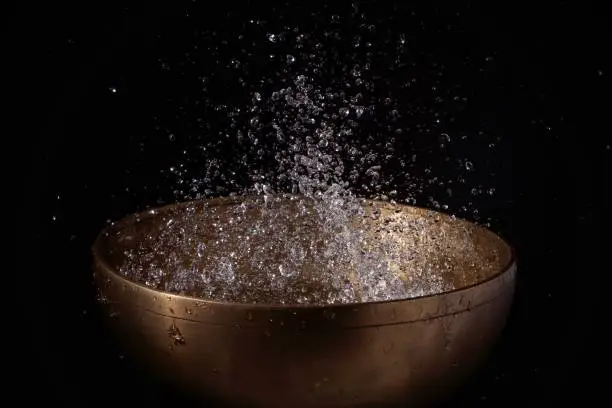 water droplets floating above the tibetan therapeutic sound bowl on a black background