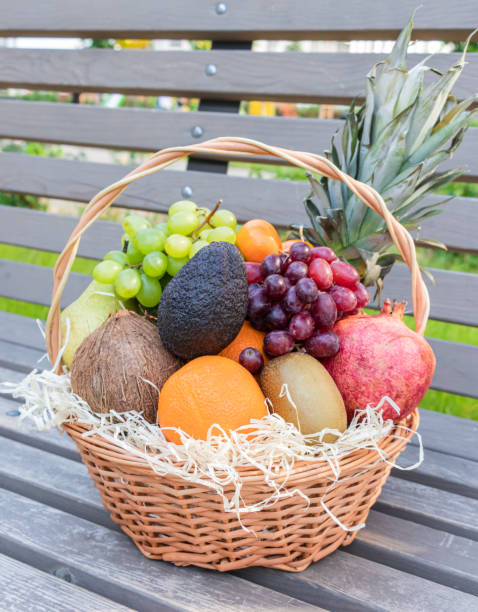 新鮮な果物やベリーでいっぱいの丸い籐のバスケットは、木製のベンチに立っています - plum fruit basket wicker ストックフォトと画像