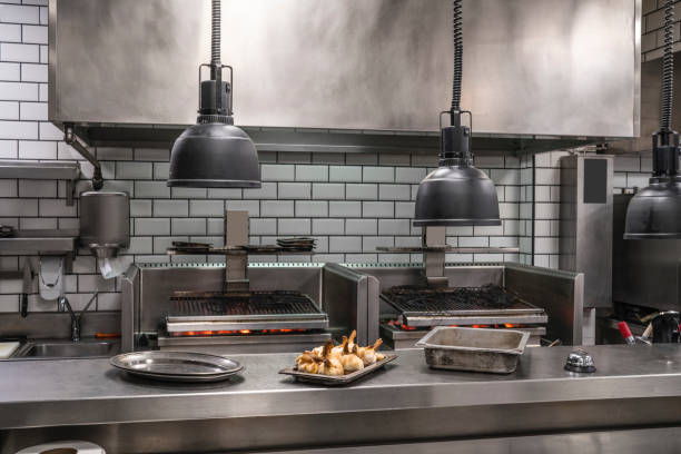 Professional restaurant stainless steel kitchen with coal embers grill Professional restaurant stainless steel kitchen with coal embers grill and roasted garlic tray in foreground garlic bulb photos stock pictures, royalty-free photos & images
