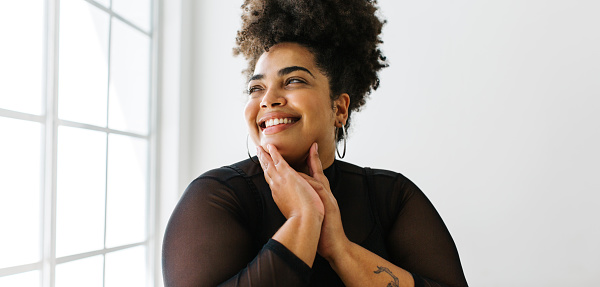 Wide angle shot of woman looking outside the window and smiling. Happy female in black casual outfit.