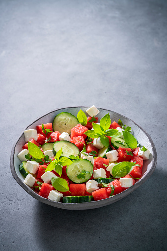 Healthy vegetarian watermelon salad bowl with feta cheese, cucumber and parsley on gray background, Mediterranean diet