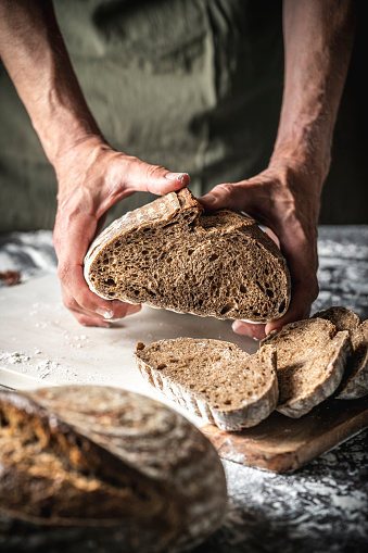 Male hands holding showing crumb of sourdough bread brown loaf wholegrain homemade German style on white flour background